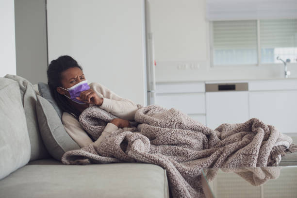 istock Ill woman with purple face mask coughing, lying down and resting. 1207990903