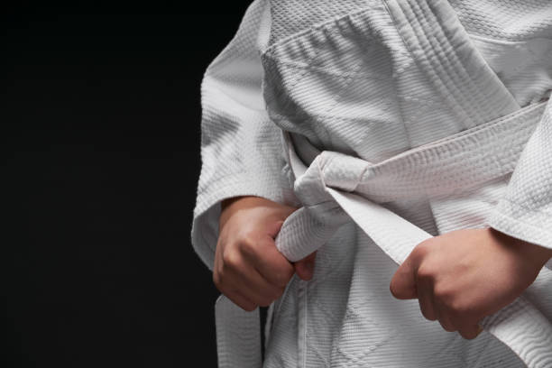 las manos primer plano - adolescente vestido con ropa de artes marciales posando sobre un fondo gris oscuro, un concepto deportivo - karate child judo belt fotografías e imágenes de stock