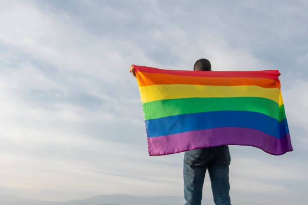 istock handsome man with gay flag on sky background 1207999641