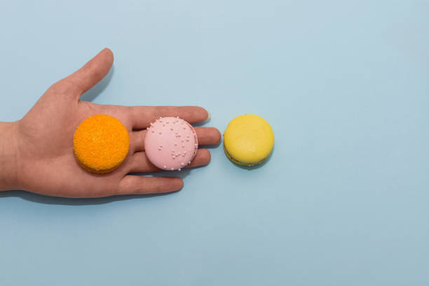 istock Macaroon cookies on female palm on blue flat background 1208012487