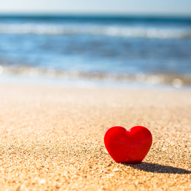 istock Romantic symbol of red heart on the sand beach 1208016109