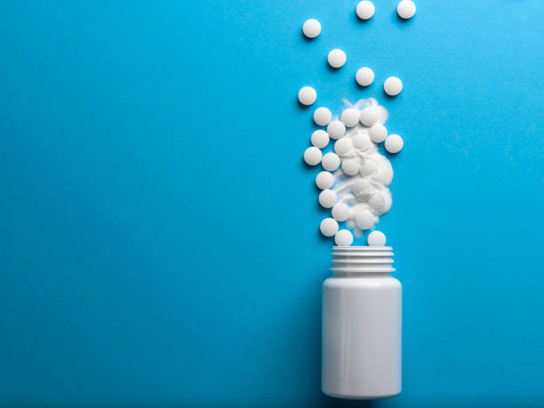istock White pills spilled from a white bottle on a blue background 1208016131