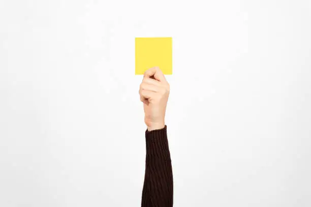 Photo of Hand of a business woman holding a yellow card in the air, white background. Authority concept.