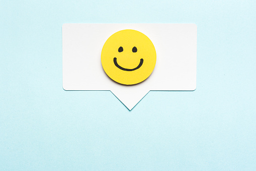 Happy face emoticon smiling comment on speech bubble and blue background. Social media marketing concept.