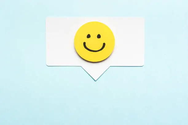 Happy face emoticon smiling comment on speech bubble and blue background. Social media marketing concept.