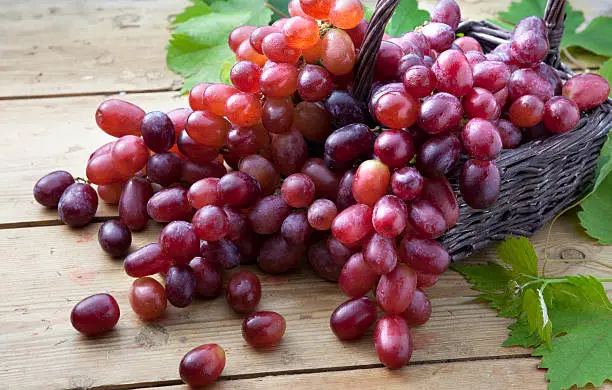 Photo of Red grapes in braided basket on wooden table