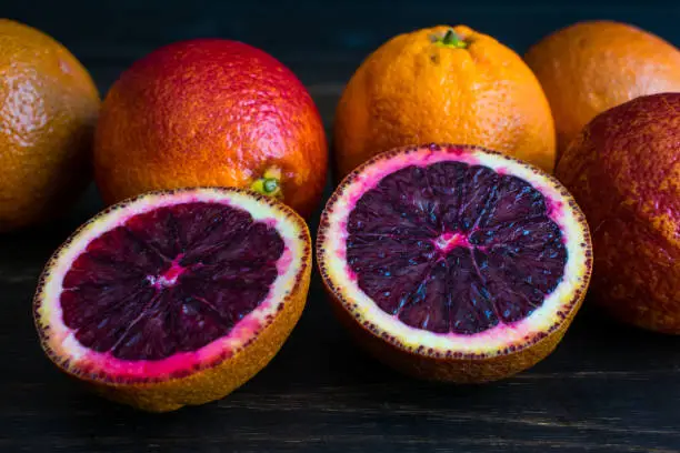 A group of blood oranges with a sliced citrus fruit in front