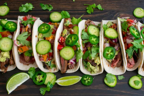 Beef tacos in flour tortillas topped with cilantro, cucumber, and jalapeños