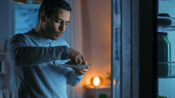 istock At Night in the Kitchen Handsome Attractive Young Man is Eating a Leftover Pizza from the Fridge. He is Hungry and Feels Satisfied. 1208033061