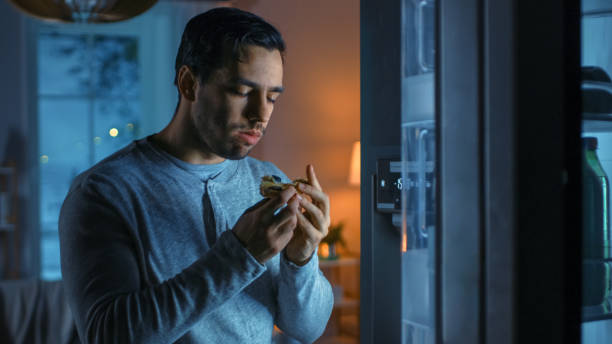 istock At Night in the Kitchen Handsome Attractive Young Man is Eating a Leftover Pizza from the Fridge. He is Hungry and Feels Satisfied. 1208033109