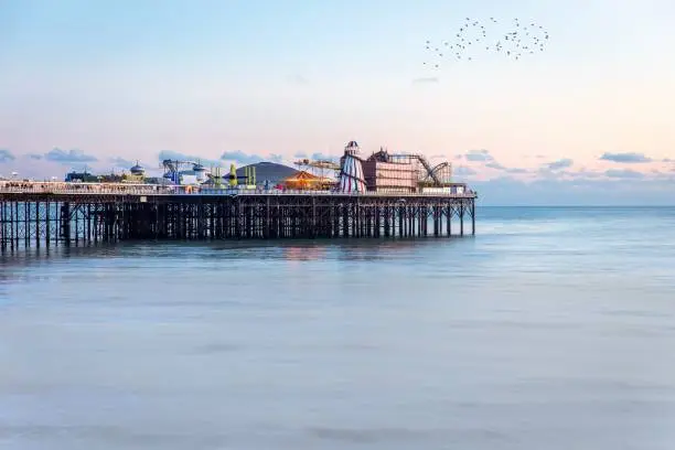 Brighton Pier in winter with blue skies and sea, starlings flying overhead and the sun setting leaving an orange glow.