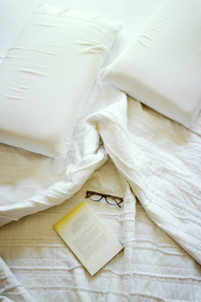 istock Book and reading glasses upon the bed with sheets 1208045927