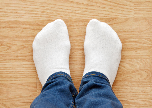 Closeup of a man's feet with new white socks on a hardwood floor.