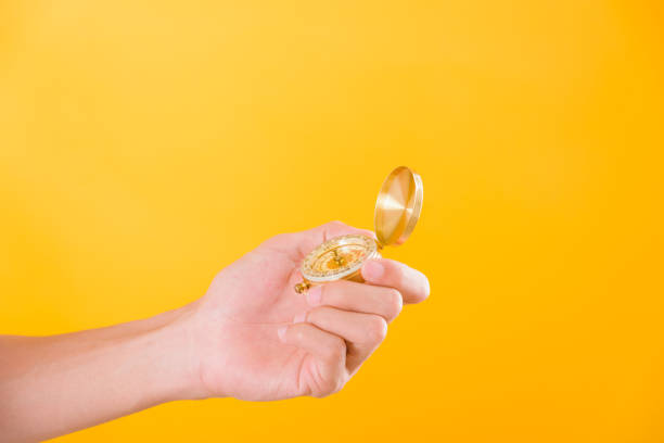 istock Hand holding antique brass compass isolated on yellow background 1208064989