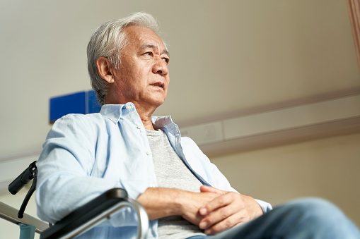 elderly asian man sitting in wheelchair in nursing home with serious facial expression