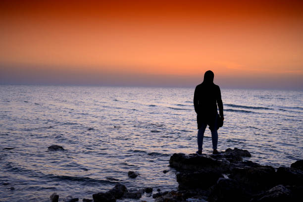istock silhouette man standing on the rock over sea and sunset 1208079919