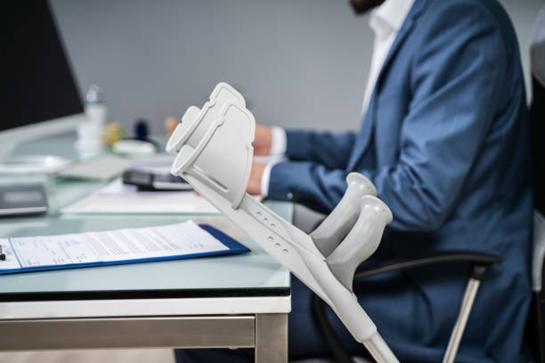 Close-up Of Crutches Leaning On Table In Front Of Handicapped Man Filling Form