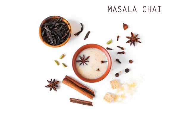 Masala Chai Tea in ceramic cup with ingredients. Traditional indian spicy black tea with milk isolated on white background, top view, copy space.