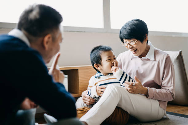 abuelos asiáticos alegres sentados en el suelo en la sala de estar charlando y jugando con el pequeño nieto juntos - whispering grandparent child grandfather fotografías e imágenes de stock