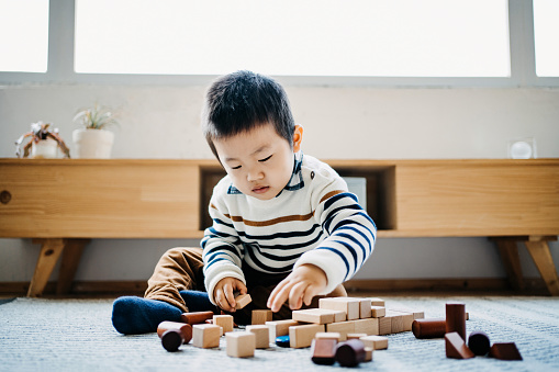 Cute little boy sitting on the floor in the living room playing wooden building blocks