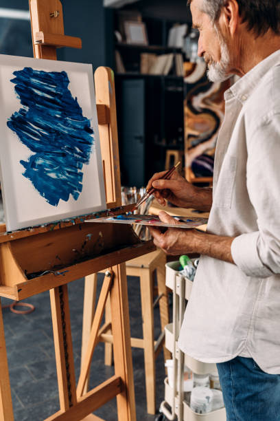 istock Senior painter standing in front of easel holding a paintbrush and palette 1208097182