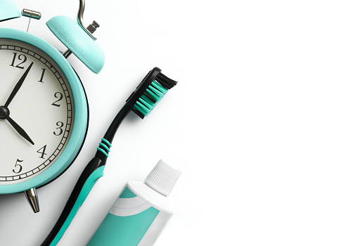 Turquoise toothbrush, alarm clock and toothpaste on white background. Dental care concept. Top view