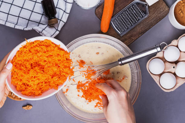 mains de femme ajoutant la carotte râpée dans un bol avec d’autres ingrédients - muffin food rustic table photos et images de collection