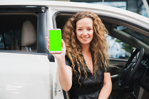 The woman sitting in the car and showing her smart phone with green screen. Automobile Application. Auto Leasing Business. Digital Business.