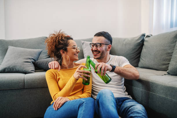 Young handsome couple relaxing at home. They are toasting with beer. Sunday afternoon. Young handsome couple relaxing at home. They are toasting with beer. Sunday afternoon. beer alcohol stock pictures, royalty-free photos & images
