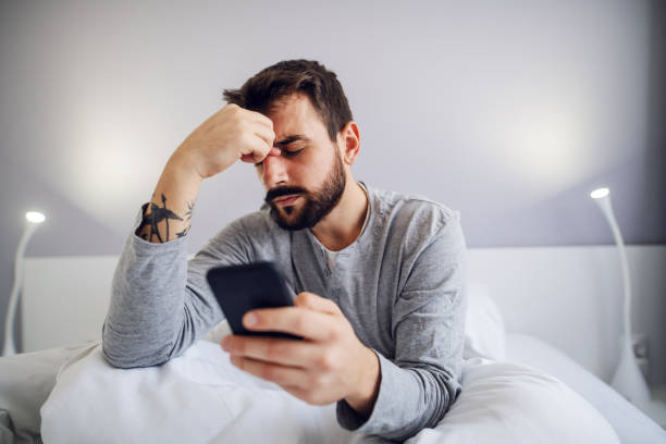 istock Young handsome bearded man sitting in bedroom, holding smart phone and getting nervous about message he received from his girlfriend. 1208103473
