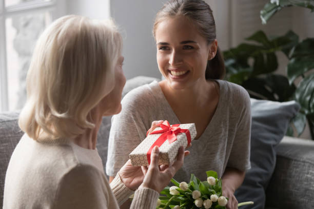 middle aged mother receiving from grown up daughter gift box - mother gift imagens e fotografias de stock