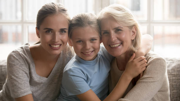 istock Three generations of women sitting on couch looking at camera 1208113598