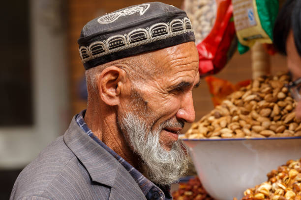 KASHGAR, XINJIANG / China - October 4, 2017: Profile of elderly, uyghur man with long, grey beard. He is wearing a traditional doppa (hat). Captured at a bazaar. Muslim uyghur minority in Xinjiang.