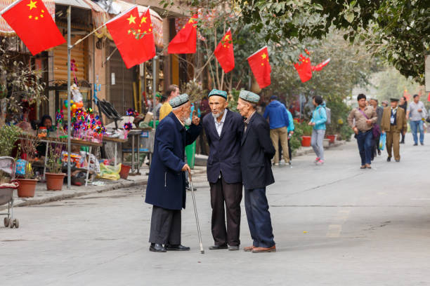 tre anziani, uiguri che hanno una conversazione. sul retro bandiere cinesi. - uighur foto e immagini stock
