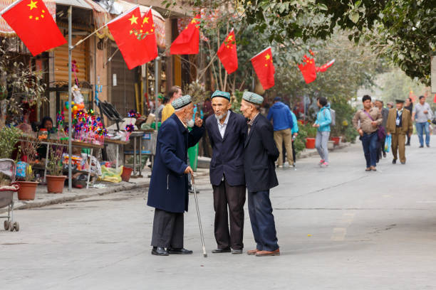 trzech starszych, ujgurskich mężczyzn rozmawia. z tyłu chińskie flagi. - west china zdjęcia i obrazy z banku zdjęć