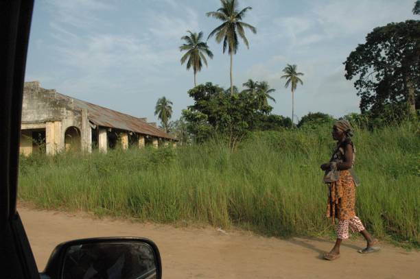 afrykańska kobieta idzie ulicą z wysoką zieloną łąką, palmami i afrykańskim kościołem. 11 lutego 2018 pointe noire, kongo. - pointe noire zdjęcia i obrazy z banku zdjęć