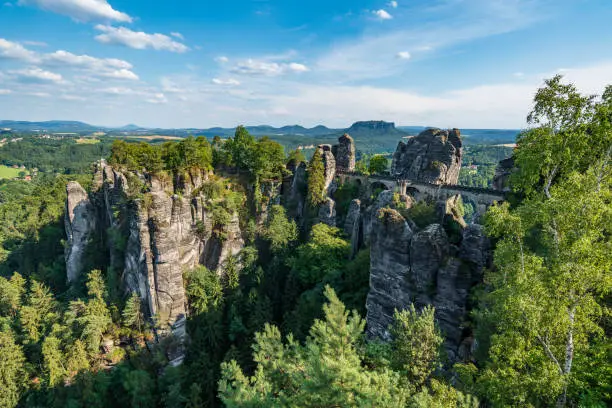 Bad Schandau in Bohemian Switzerland. Bastei bridge and mountain view. Narrow rock, natural sandstone arch in Europe."nHill scenery with greenery, blue sky and sunlight.