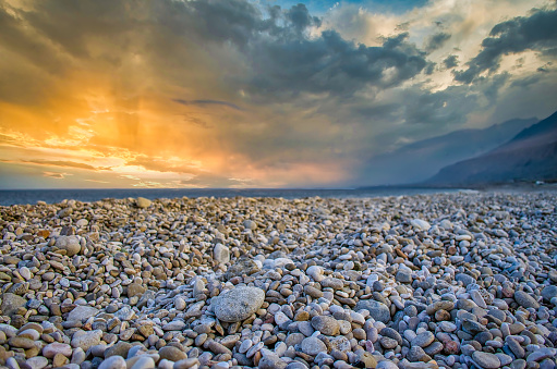 Low Angle shot of pebble beach bathed in orange light during sunset. From Sur, Muscat, Oman.