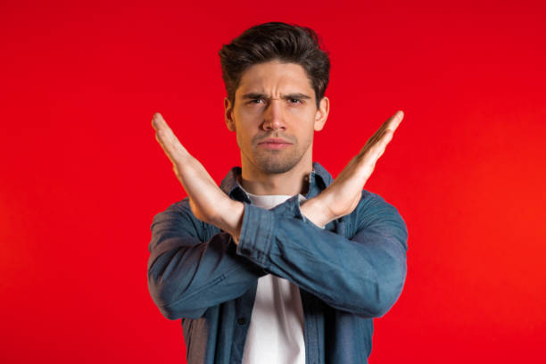istock Man disapproving with no crossing hands sign make negation gesture. Denying, Rejecting, Disagree, Portrait of handsome guy on red background 1208129697
