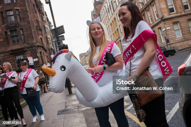 A Bride Wearing A Unicorn Head Piece With A Veil And Unicorn Floatation Device Walks The Streets Of Glasgow With Her Friends At Her Henparty Prior To Her Wedding Stock Photo - Download Image Now