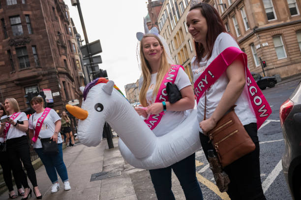 uma noiva, usando uma peça de cabeça de unicórnio com um véu e dispositivo de flutuação de unicórnio, anda pelas ruas de glasgow com seus amigos em sua festa de galinha, antes de seu casamento. - stag night fotos - fotografias e filmes do acervo