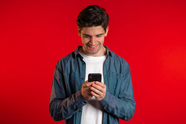 istock Man sms texting using app on smartphone. Handsome young guy surfing internet with mobile phone. Red studio 1208130612