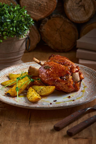 istock Pork knuckle with baked potatoes on rustic kitchen table at dark wooden background, front view. Pork leg done, German food 1208130806