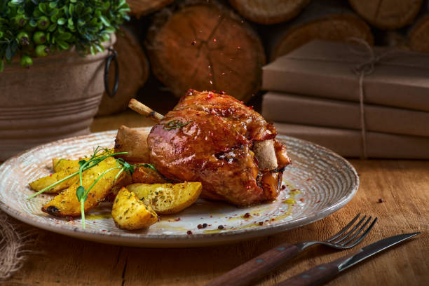 istock Pork knuckle with baked potatoes on rustic kitchen table at dark wooden background, front view. Pork leg done, German food 1208130808