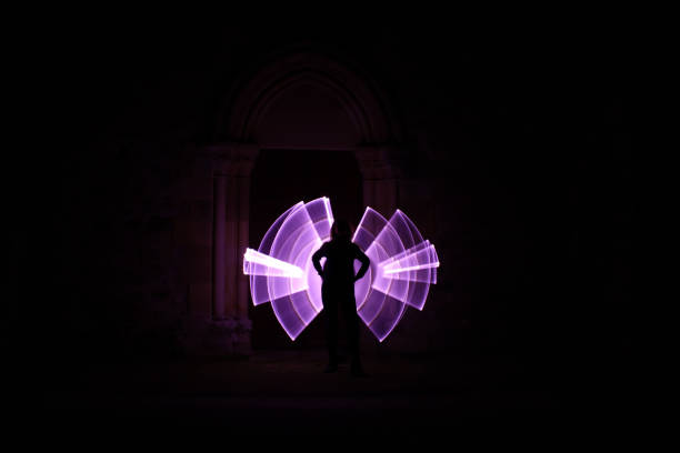 Lightpainting session at night. Silhouette of woman standing from the front. Curved abstract shapes made of violet light saber in background. Mode long exposure. lightpainting stock pictures, royalty-free photos & images