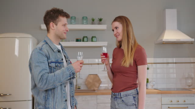 couple in love stands in the kitchen with champagne in their hands and the girlfriend says a toast