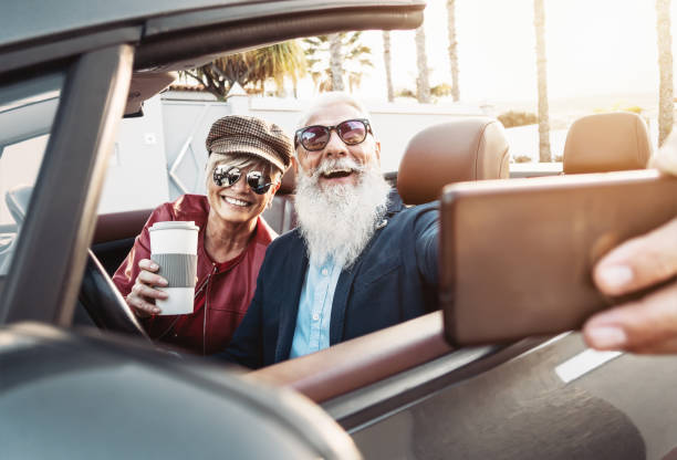 szczęśliwa starsza para robiąca selfie na nowym nowoczesnym kabriolecie - dojrzali ludzie bawiący się razem robiąc sobie zdjęcia podczas wakacji - starszy styl życia i koncepcja transportu podróżniczego - outdoors car convertible wealth zdjęcia i obrazy z banku zdjęć