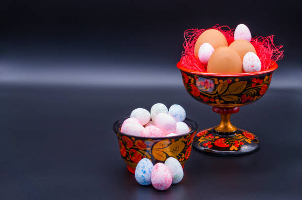Unusual Easter on a dark background. Brown eggs in a Khokhloma vase and small multi-colored eggs in a Khokhloma bowl on a black background.