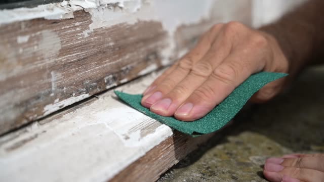 Slow motion shot of a man's hand sanding the edge of a worn window sill