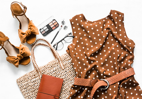 Vestido marrón verano lunar, sandalias de cuña de ante, bolso de mano de paja ecológica, cosméticos sobre un fondo claro, vista superior. Juego de ropa de mujer photo
